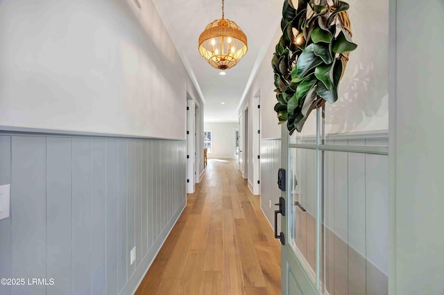 hallway featuring light wood-type flooring, wainscoting, and an inviting chandelier