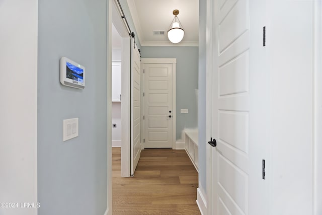 hallway featuring a barn door, visible vents, baseboards, light wood finished floors, and crown molding