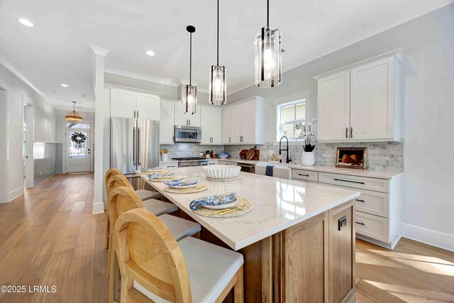 kitchen featuring a center island, white cabinetry, appliances with stainless steel finishes, light stone countertops, and decorative light fixtures