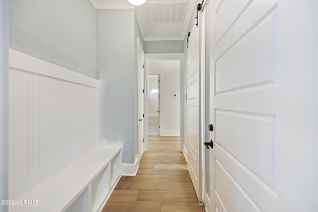 corridor with light wood finished floors, visible vents, a barn door, ornamental molding, and baseboards