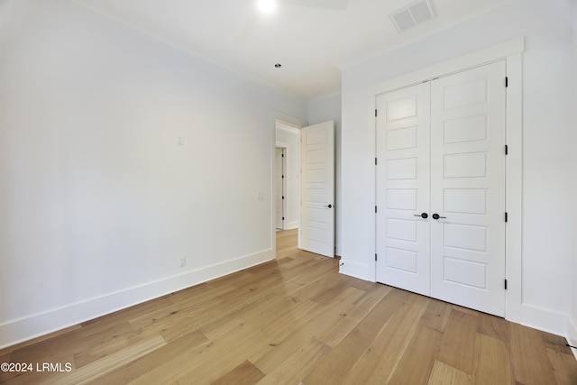 unfurnished bedroom with visible vents, baseboards, a closet, light wood finished floors, and crown molding