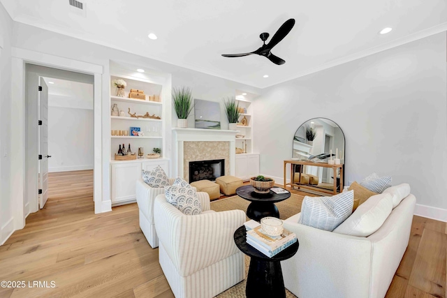 living room with built in shelves, a fireplace, ceiling fan, light wood-type flooring, and baseboards