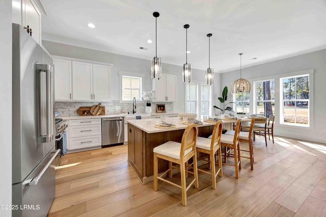 kitchen featuring stainless steel appliances, a kitchen island, white cabinets, backsplash, and pendant lighting