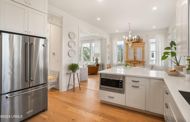 kitchen featuring light hardwood / wood-style flooring, appliances with stainless steel finishes, white cabinetry, hanging light fixtures, and an inviting chandelier