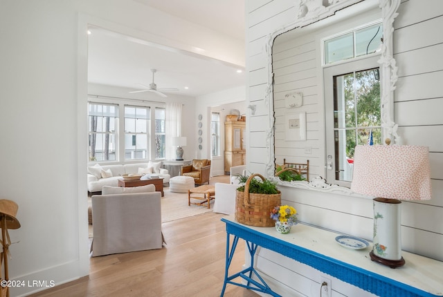 living room featuring ceiling fan, light hardwood / wood-style floors, and wood walls