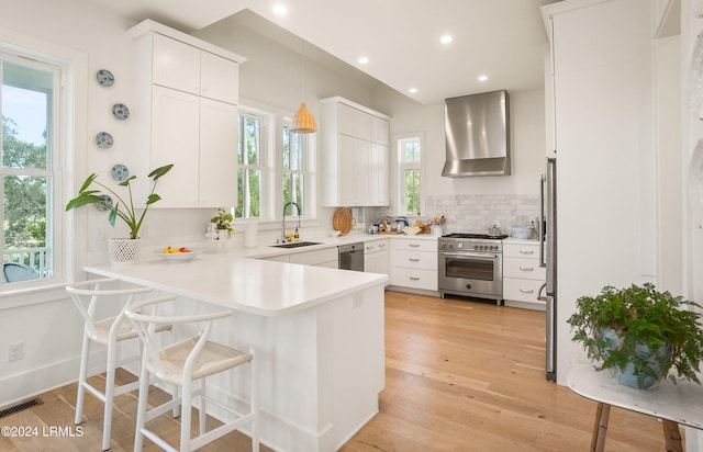 kitchen with white cabinetry, decorative light fixtures, stainless steel appliances, and wall chimney exhaust hood