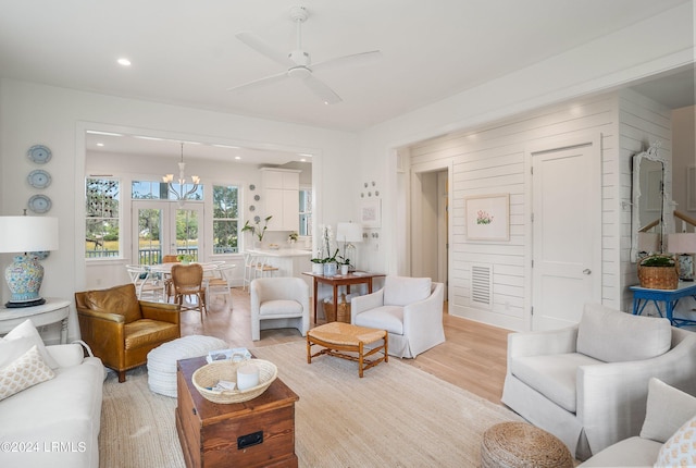 living room featuring ceiling fan with notable chandelier and light wood-type flooring