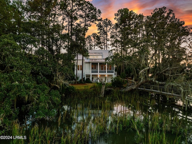 back house at dusk featuring a balcony and a water view