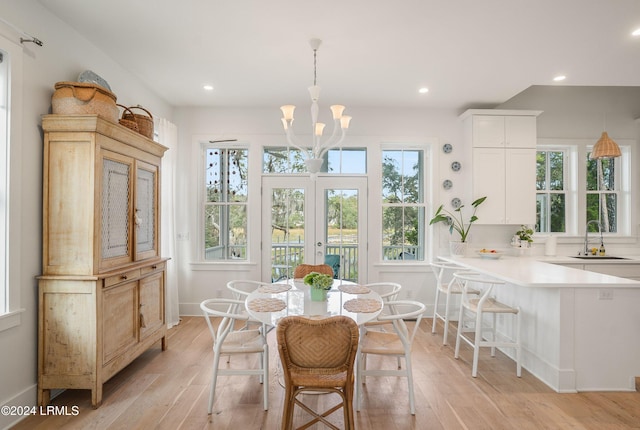 dining space featuring sink, an inviting chandelier, light hardwood / wood-style floors, and french doors