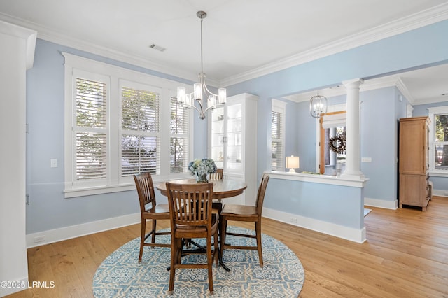 dining space featuring crown molding, a chandelier, light wood-type flooring, and ornate columns