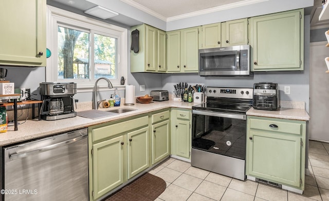 kitchen with sink, crown molding, light tile patterned floors, green cabinets, and appliances with stainless steel finishes