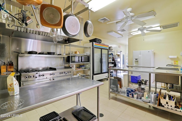 kitchen with light tile patterned floors, sink, stainless steel counters, white refrigerator with ice dispenser, and range with two ovens