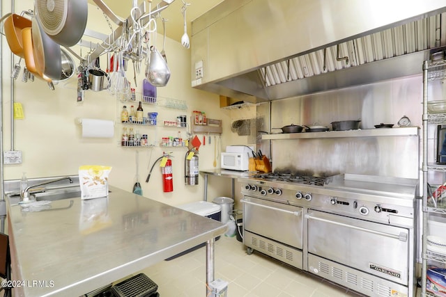 kitchen with light tile patterned floors, decorative light fixtures, wall chimney range hood, and stainless steel counters