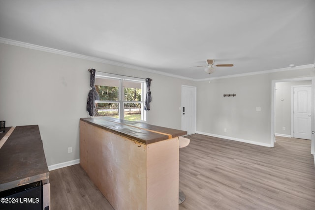 kitchen with ceiling fan, hardwood / wood-style floors, ornamental molding, a kitchen bar, and kitchen peninsula