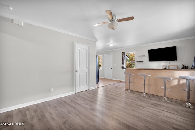 unfurnished living room with bar, ornamental molding, ceiling fan, and light wood-type flooring