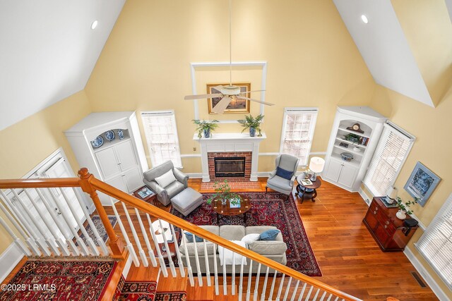 living area with a wealth of natural light, high vaulted ceiling, wood finished floors, and a brick fireplace