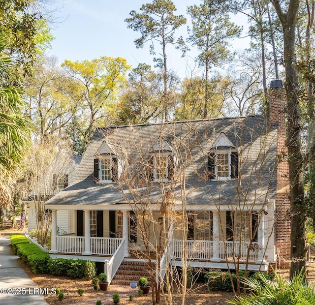 cape cod-style house featuring a chimney, a porch, and roof with shingles