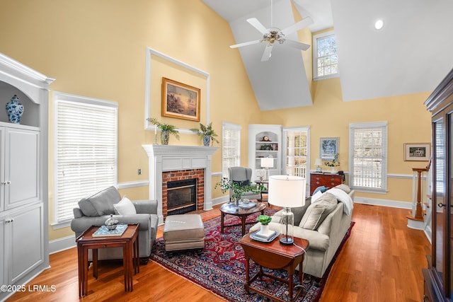 living area with high vaulted ceiling, light wood-type flooring, a ceiling fan, and a brick fireplace