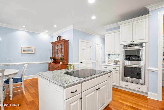 kitchen with light wood-type flooring, black electric stovetop, double oven, and a kitchen island