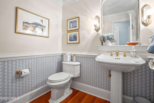 bathroom featuring a wainscoted wall, crown molding, wood finished floors, toilet, and wallpapered walls