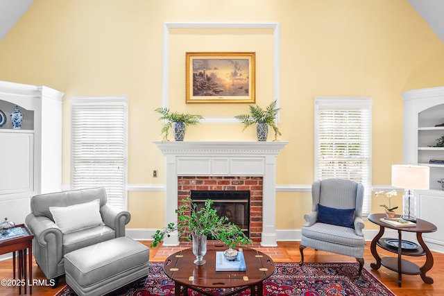 living area with baseboards, built in shelves, wood finished floors, and a brick fireplace