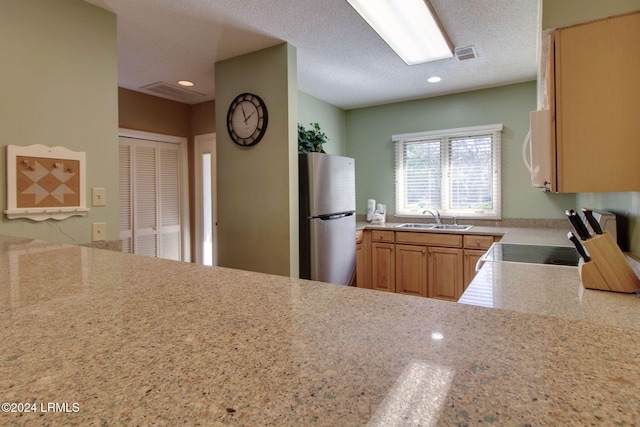 kitchen featuring stainless steel refrigerator, light stone counters, sink, and a textured ceiling