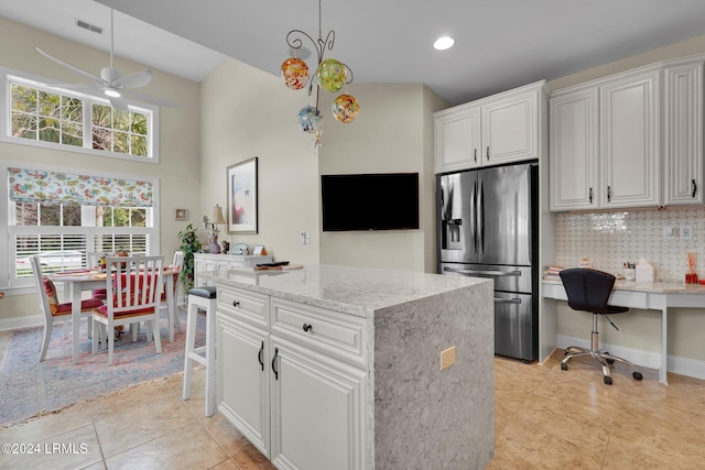 kitchen with stainless steel refrigerator with ice dispenser, tasteful backsplash, plenty of natural light, a kitchen island, and white cabinets