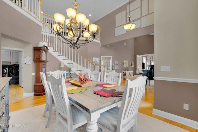 dining space with an inviting chandelier, washing machine and dryer, light hardwood / wood-style flooring, and a high ceiling