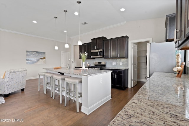 kitchen with a sink, backsplash, light stone countertops, appliances with stainless steel finishes, and dark wood finished floors