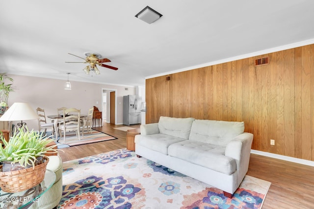 living room with ceiling fan, ornamental molding, hardwood / wood-style floors, and wood walls