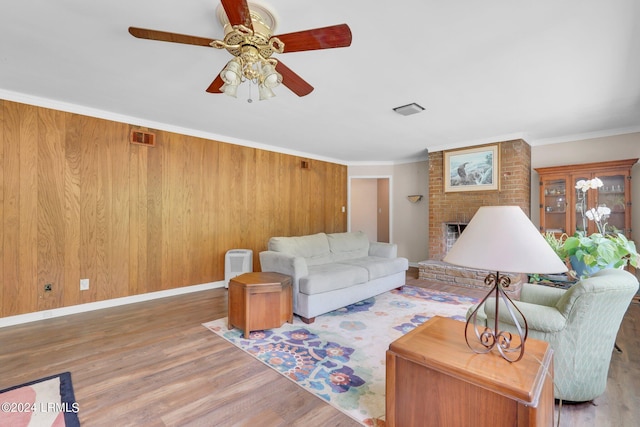 living room with crown molding, a brick fireplace, wood-type flooring, and ceiling fan