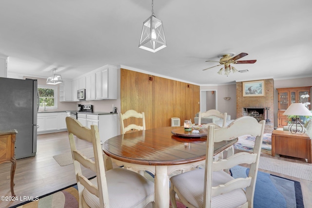 dining space with sink, light hardwood / wood-style flooring, ceiling fan, a fireplace, and ornamental molding