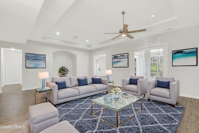 living room featuring a raised ceiling, dark wood-type flooring, ceiling fan, and french doors