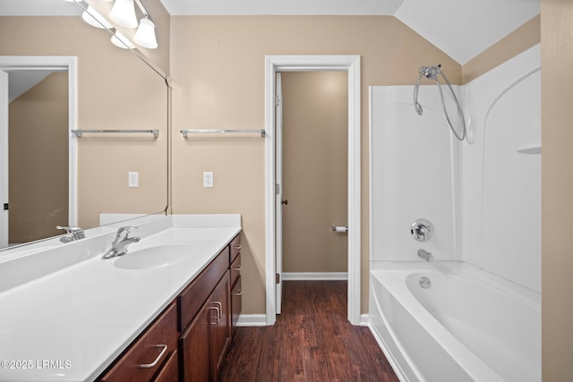 bathroom featuring lofted ceiling, wood finished floors, vanity, baseboards, and  shower combination