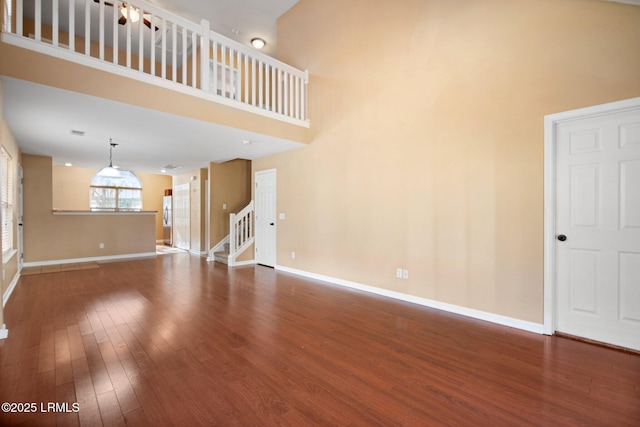 unfurnished living room featuring stairs, wood finished floors, a towering ceiling, and baseboards