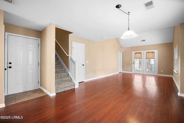 unfurnished living room featuring baseboards, visible vents, stairway, wood finished floors, and vaulted ceiling