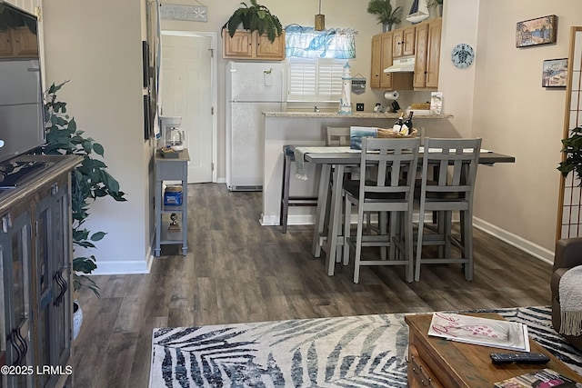 kitchen featuring white refrigerator, a kitchen bar, dark wood-type flooring, and pendant lighting