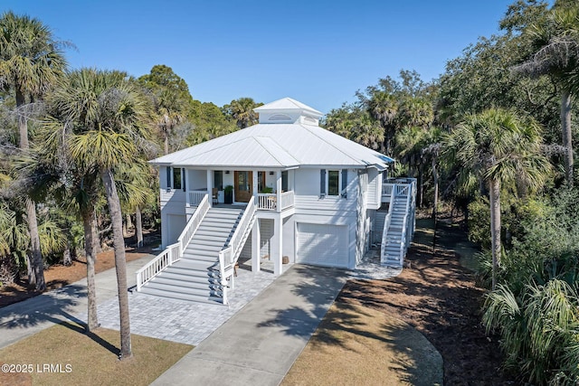 coastal home with a garage, covered porch, concrete driveway, and stairs