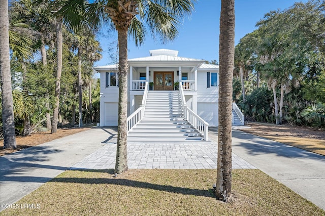 coastal inspired home with driveway, metal roof, covered porch, stairs, and french doors