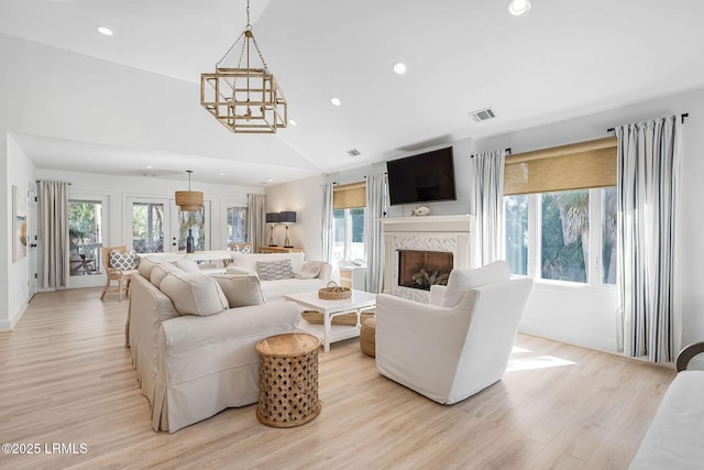 living area with a high end fireplace, light wood-type flooring, visible vents, and vaulted ceiling