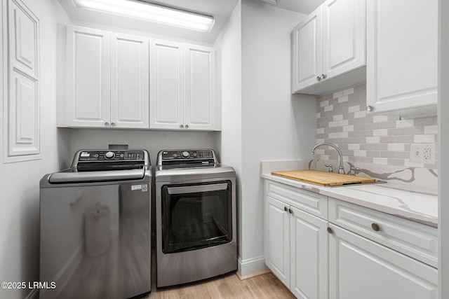 washroom with washing machine and clothes dryer, light wood-type flooring, a sink, and cabinet space