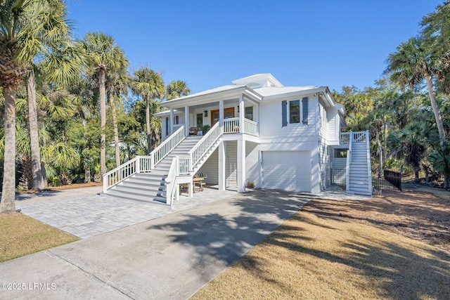 beach home with stairs, concrete driveway, a porch, and an attached garage