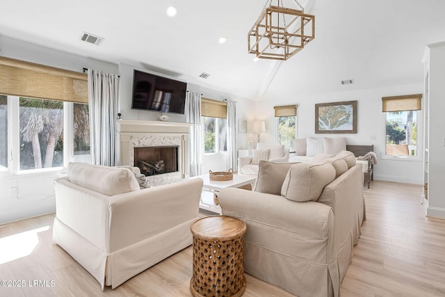 living area with light wood-style floors, a chandelier, visible vents, and a premium fireplace