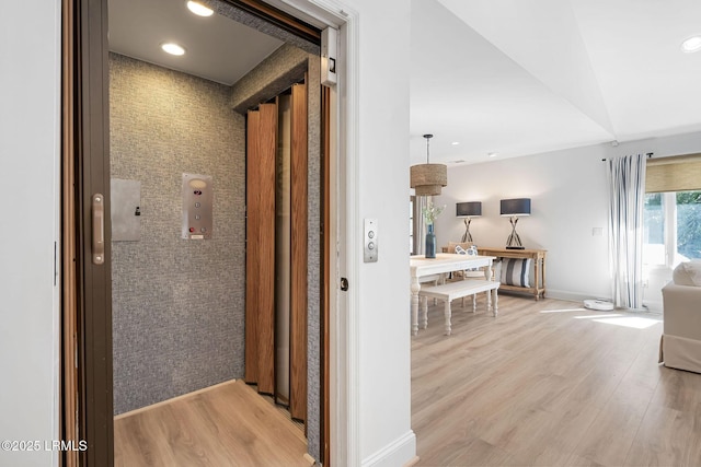 corridor with light wood finished floors, recessed lighting, an accent wall, elevator, and baseboards