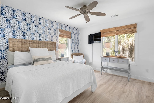 bedroom with baseboards, visible vents, ceiling fan, an accent wall, and light wood-type flooring