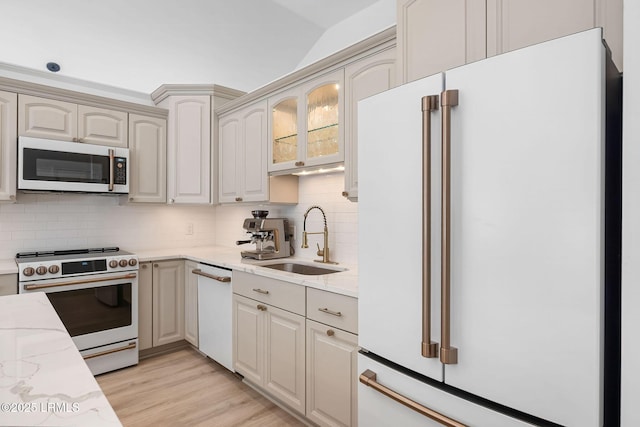 kitchen featuring light stone counters, white appliances, a sink, light wood-type flooring, and backsplash