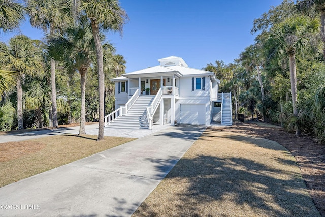 coastal inspired home featuring covered porch, driveway, an attached garage, and stairs