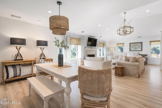 dining room with a fireplace, visible vents, an inviting chandelier, vaulted ceiling, and light wood-type flooring