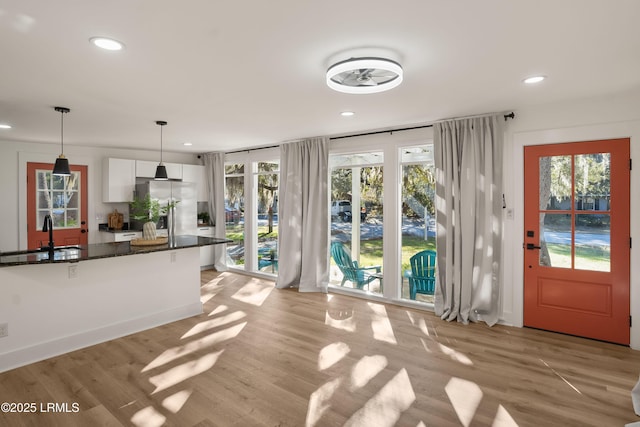 kitchen featuring sink, white cabinets, hanging light fixtures, stainless steel fridge with ice dispenser, and light wood-type flooring