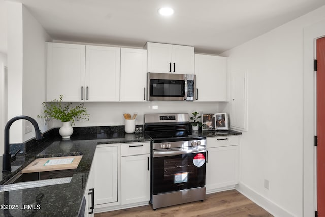 kitchen featuring sink, appliances with stainless steel finishes, dark stone countertops, light hardwood / wood-style floors, and white cabinets